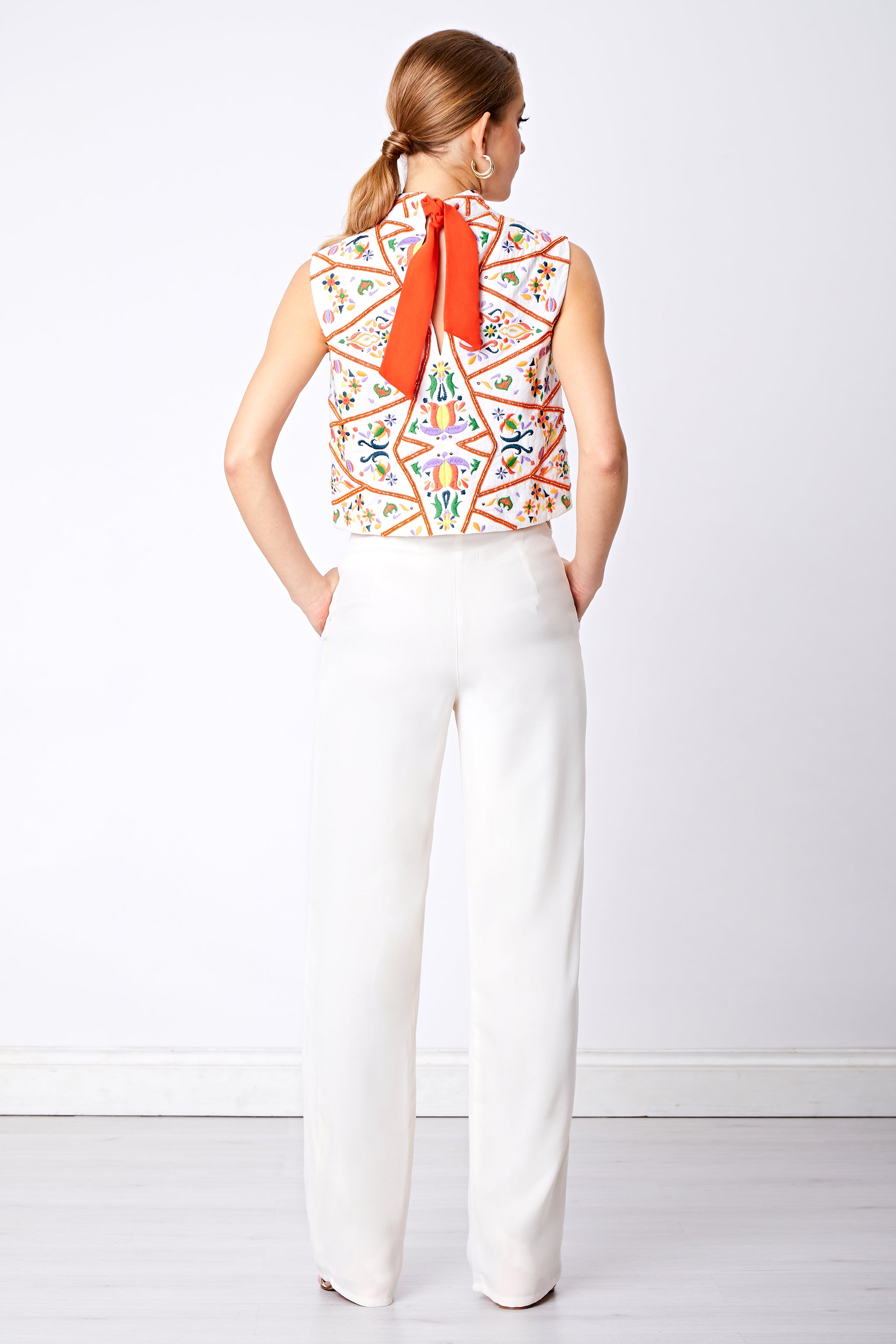 Back view of wide leg white trouser and colourful sleeveless top with orange bow detail
