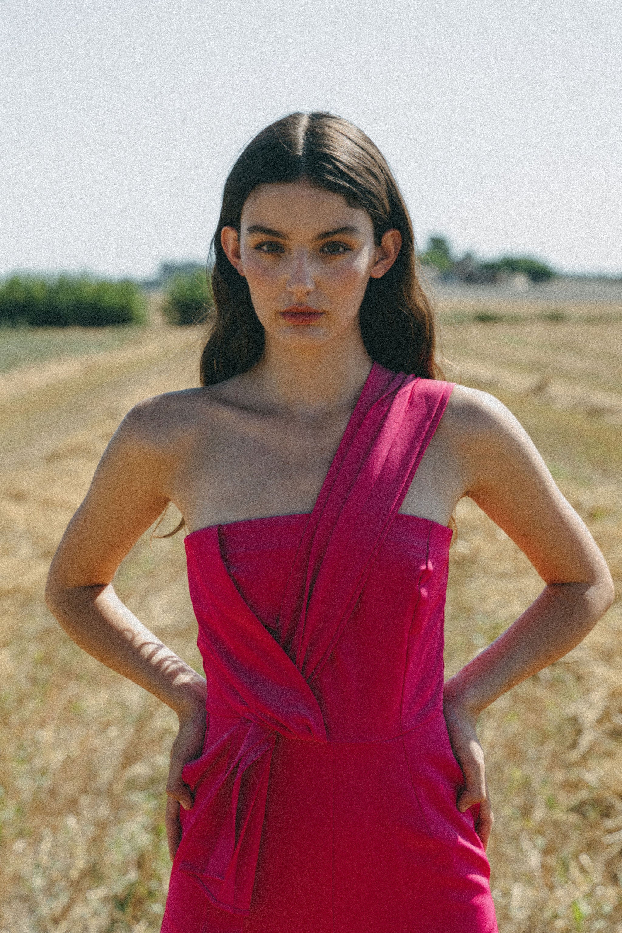 girl in field wearing a bright pink jumpsuit with pleated detail 