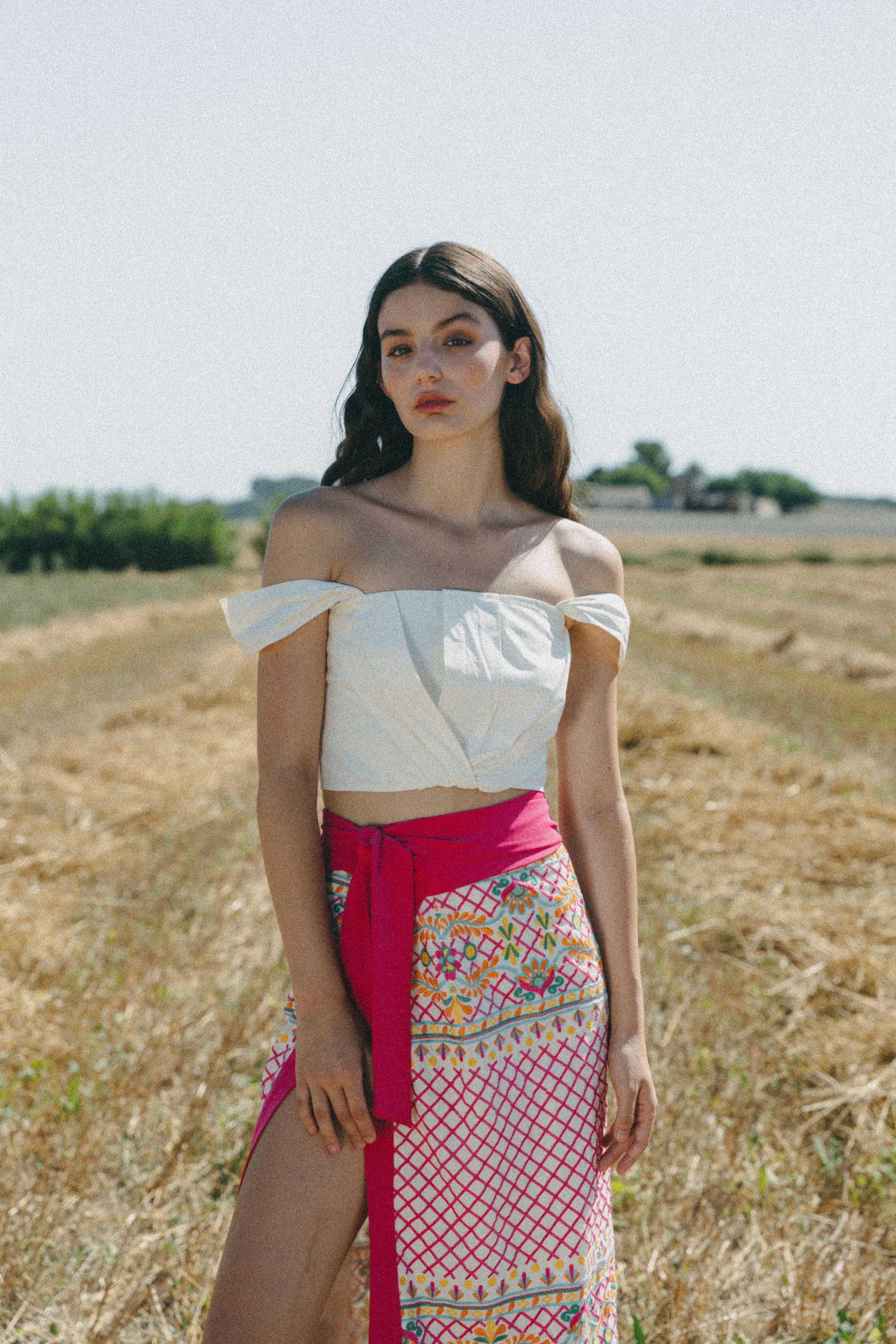 girl in field with white crop top and embroidered colourful sarong