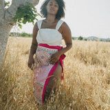 girl in field wearing white crop top and embroidered sarong with pink border