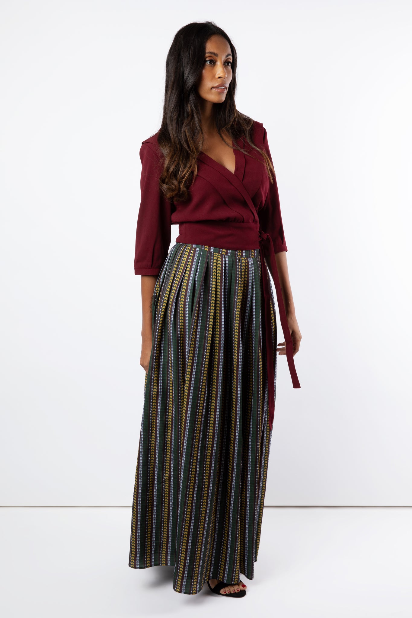 Model wears maroon pleated wrap shirt with printed maxi skirt