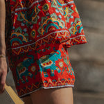 Person wearing a colorful patterned skirt with elephants, holding a book.
