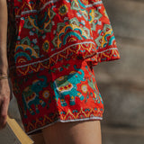 Person wearing a colorful patterned skirt with elephants, holding a book.