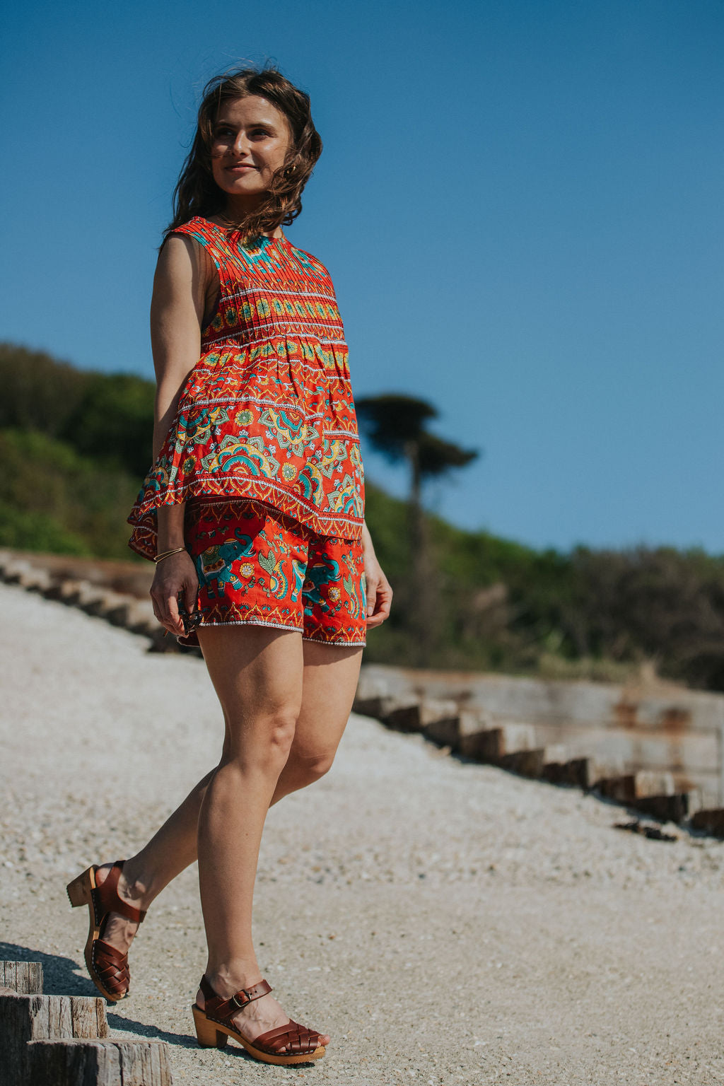 Woman in a colorful dress standing on a path with a clear blue sky and greenery in the background