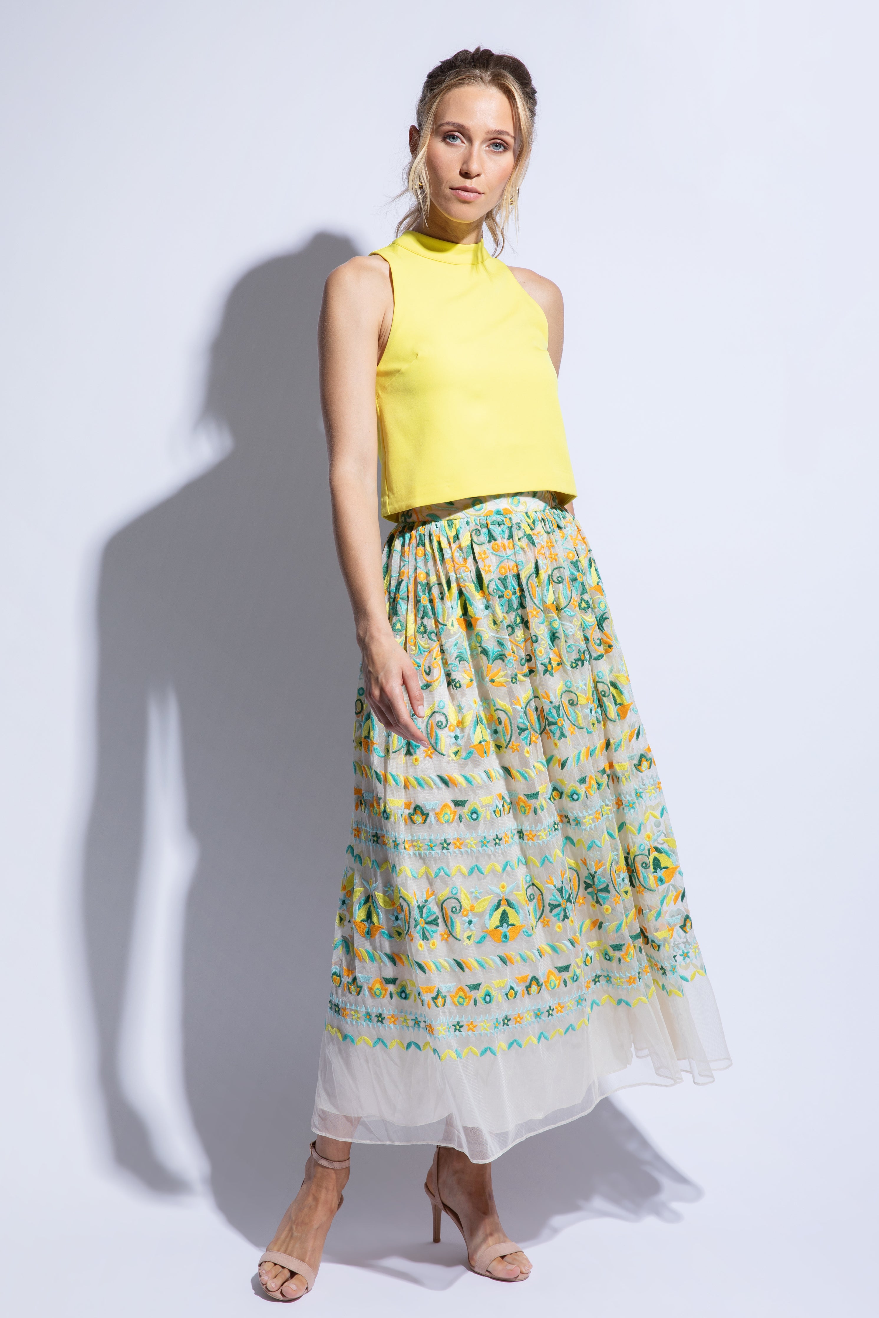 Model wears a brightly embroidered tulle skirt with yellow sleeveless top