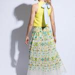 Back view of model wearing bright summer top with blue bow detail and colourful embroidered tulle skirt