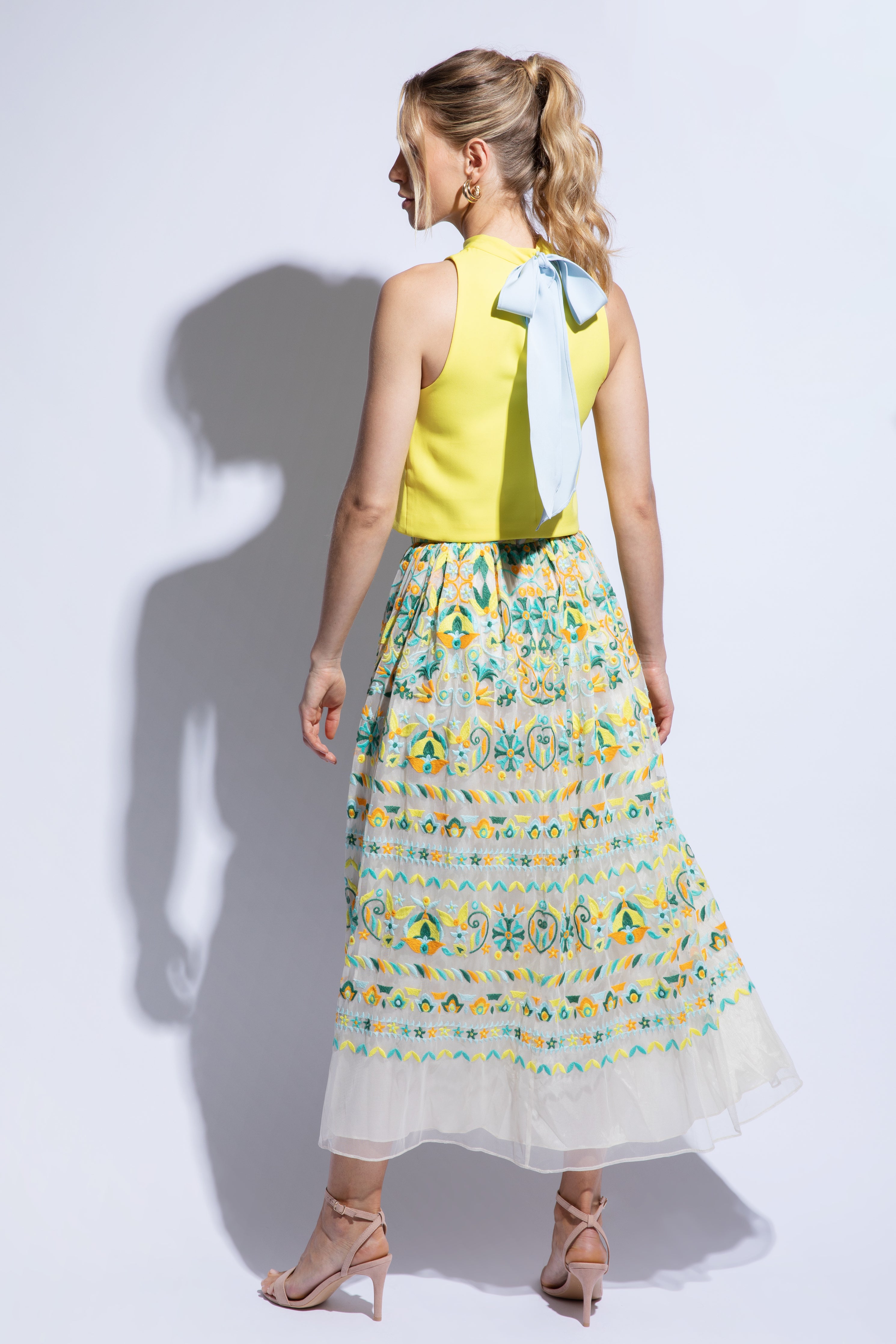 Back view of model wearing bright summer top with blue bow detail and colourful embroidered tulle skirt