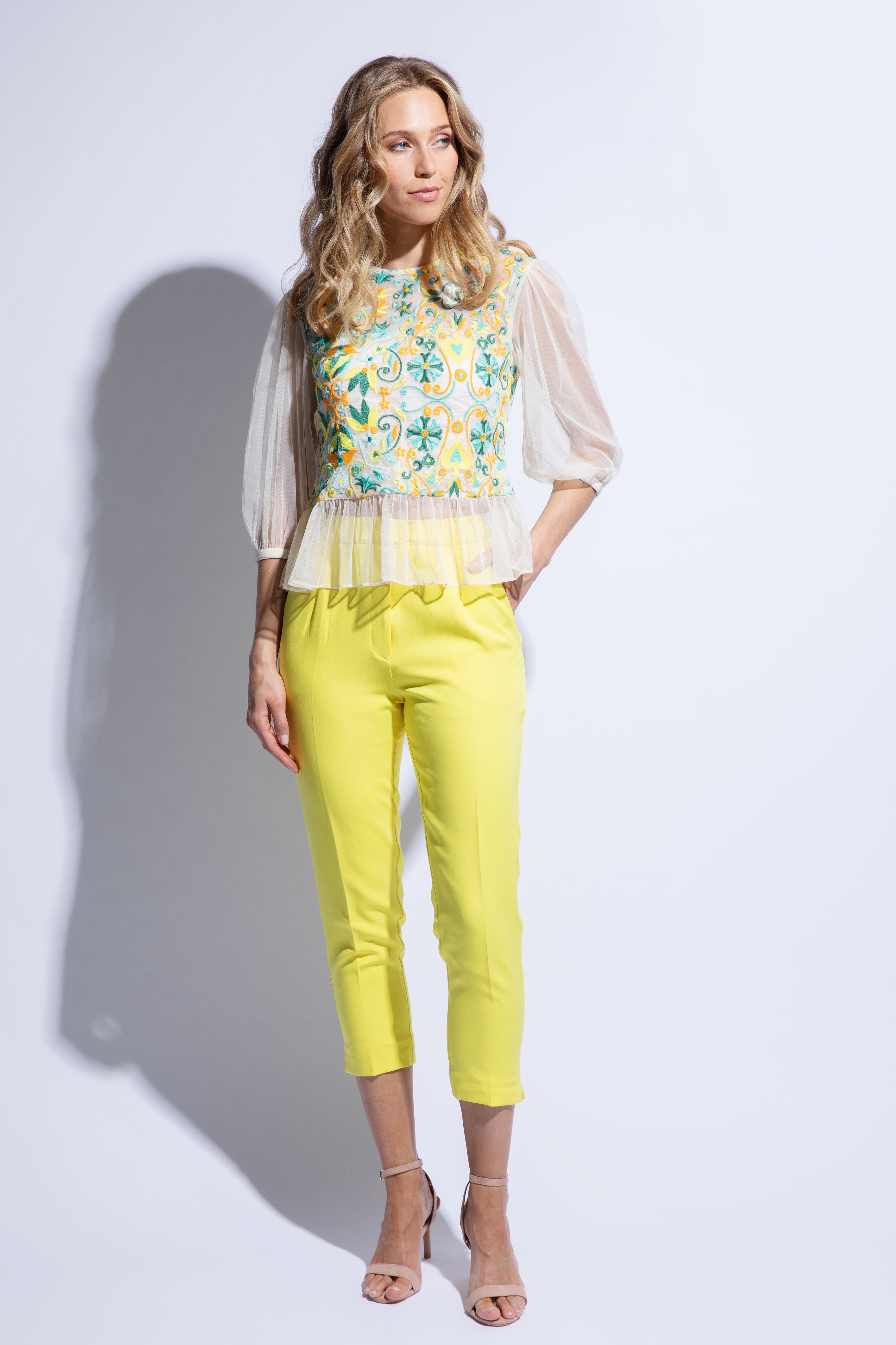 Model wears embroidered sheer top with sleeves and yellow tailored cropped trouser