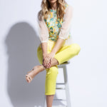 Model seated on stool wearing tulle embroidered top and bright yellow trouser