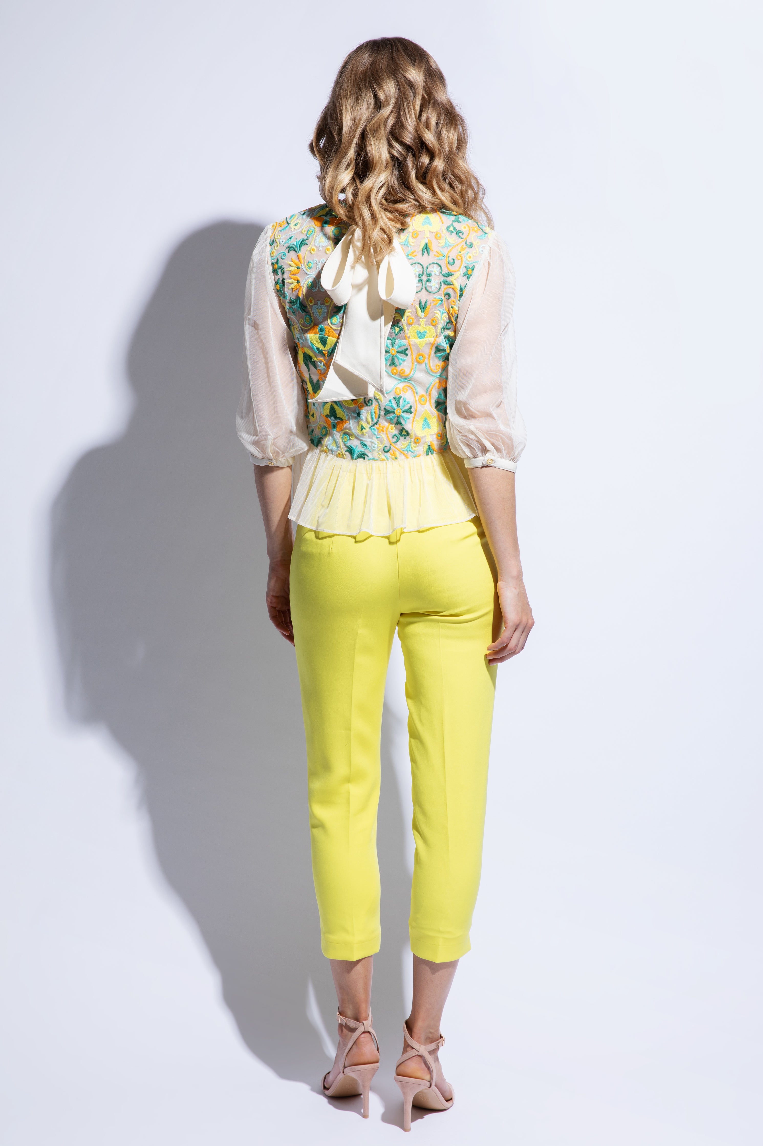 Back view of sheer embroidered and colourful top with fitted yellow trouser and bow detail