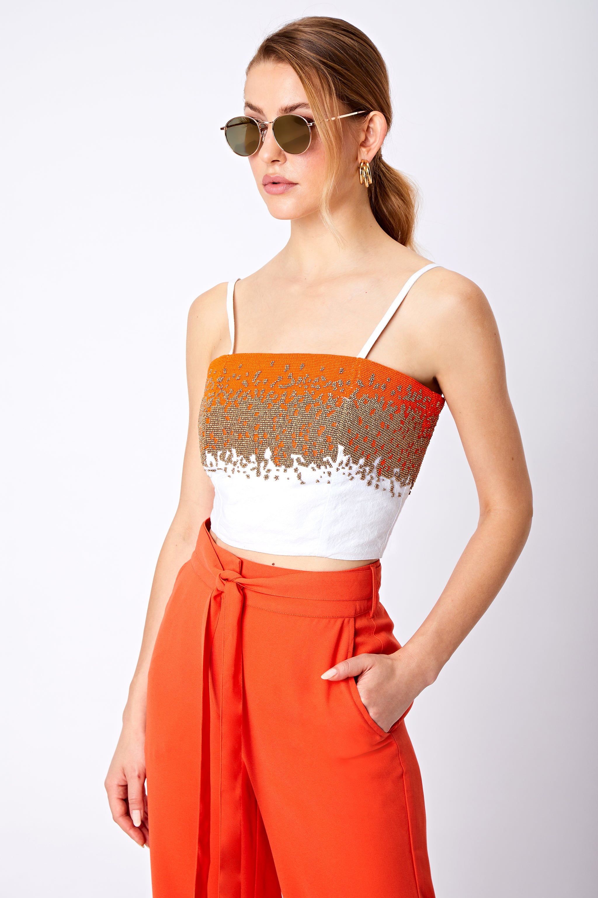 Close up beaded bralette top and orange trouser with pocket and tied belt detail