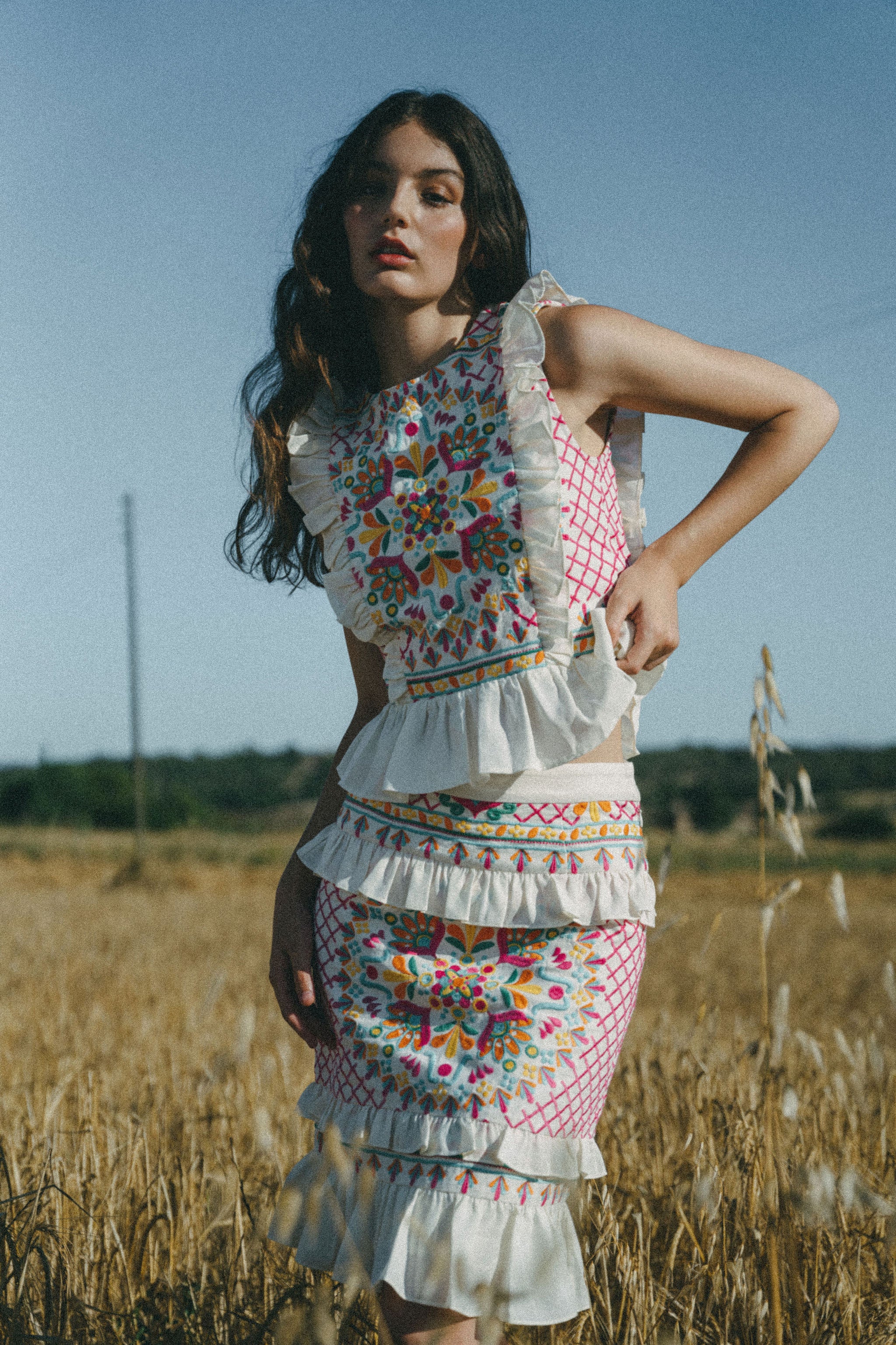 girl in field wearing colourful embroidered top and skirt with frills