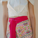 white draped top with embroidered sarong with pink tie at waist.