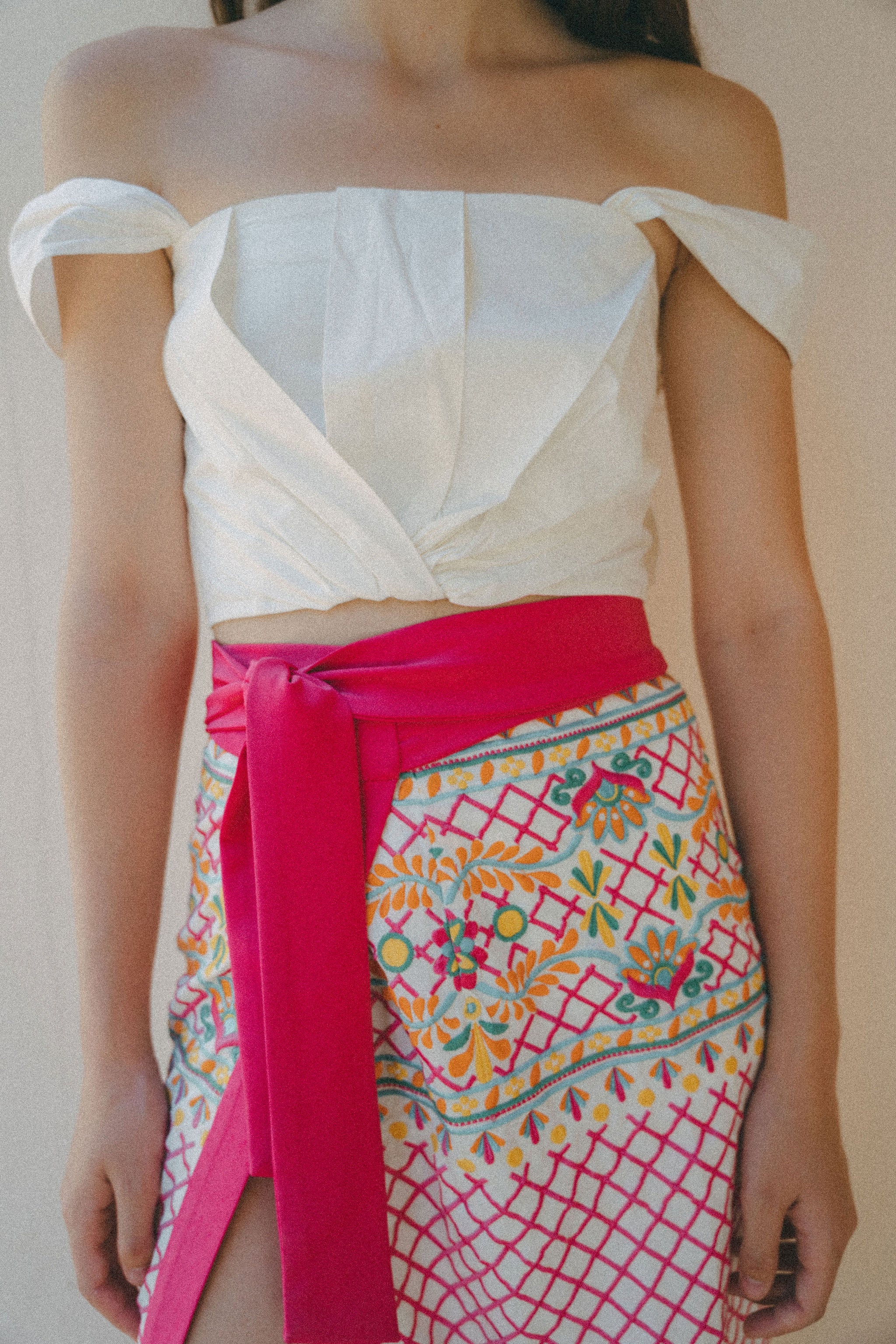 white draped top with embroidered sarong with pink tie at waist.