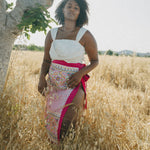 girl in field wearing white crop top and embroidered sarong with pink border