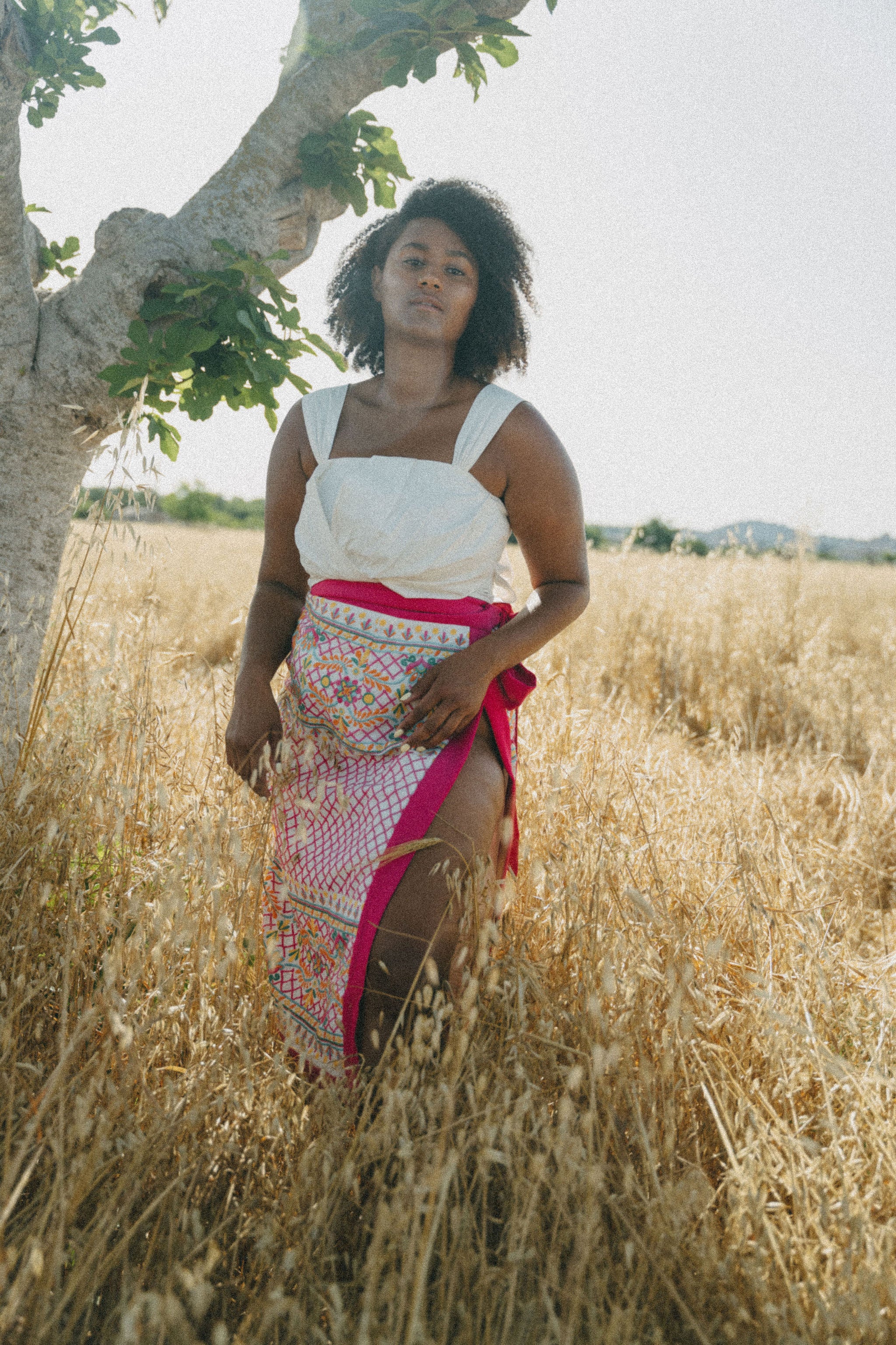 girl in field wearing white crop top and embroidered sarong with pink border