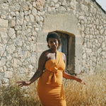 girl in field wears orange fitted dress with pleating details