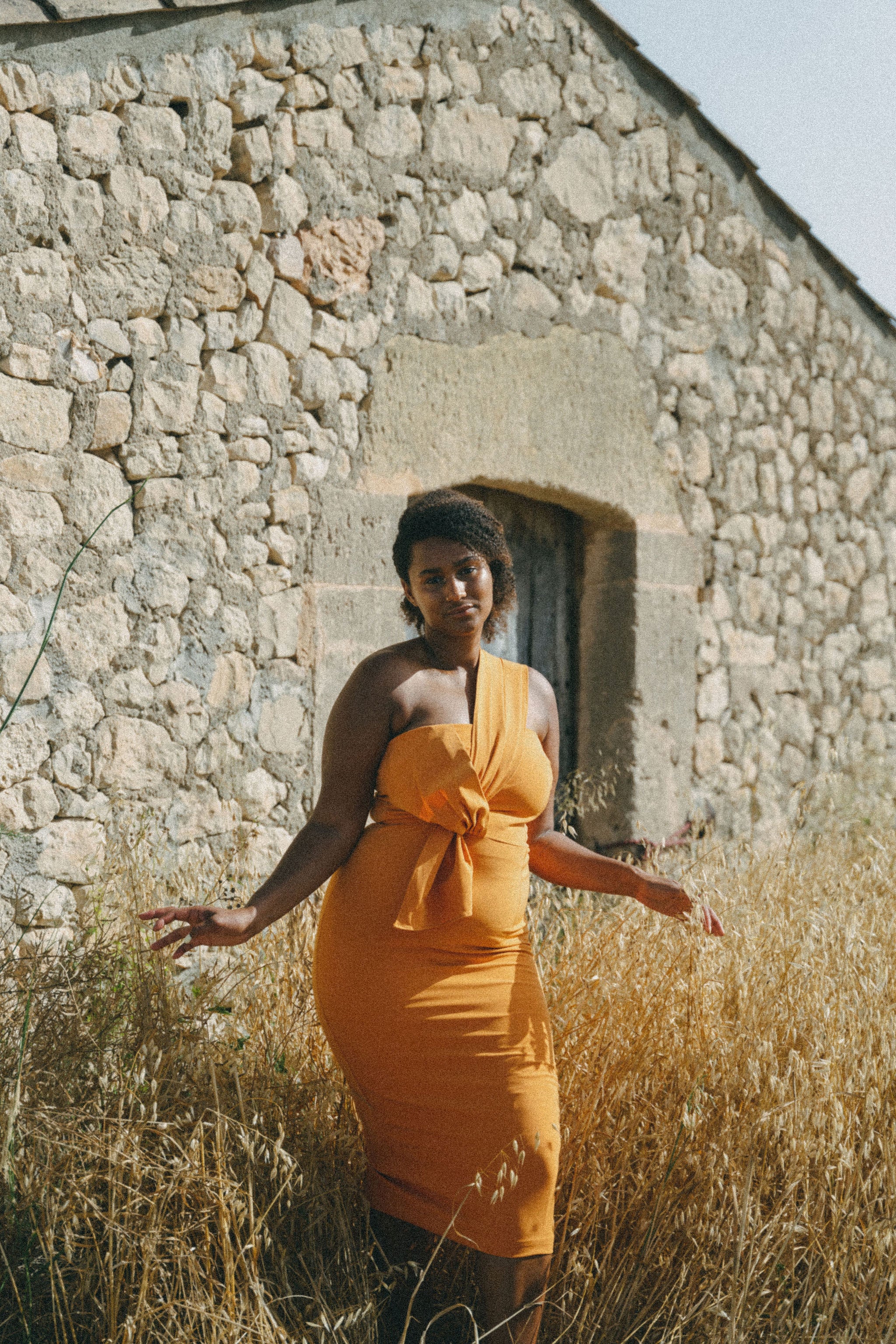 girl in field wears orange fitted dress with pleating details