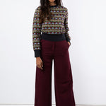 Model wears sheer embroidered jumper with wide leg maroon trouser