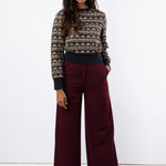 Model wears maroon wide leg trousers and embroidered tulle jumper