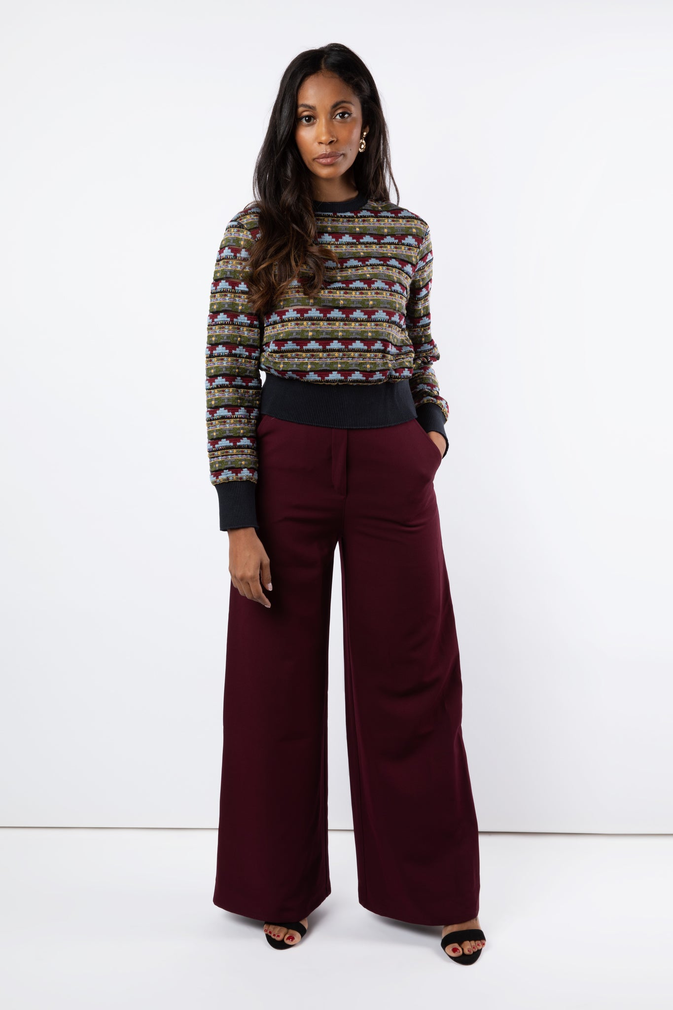Model wears maroon wide leg trousers and embroidered tulle jumper