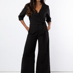 Model wears black jumpsuit with wide leg trouser and tied  belt