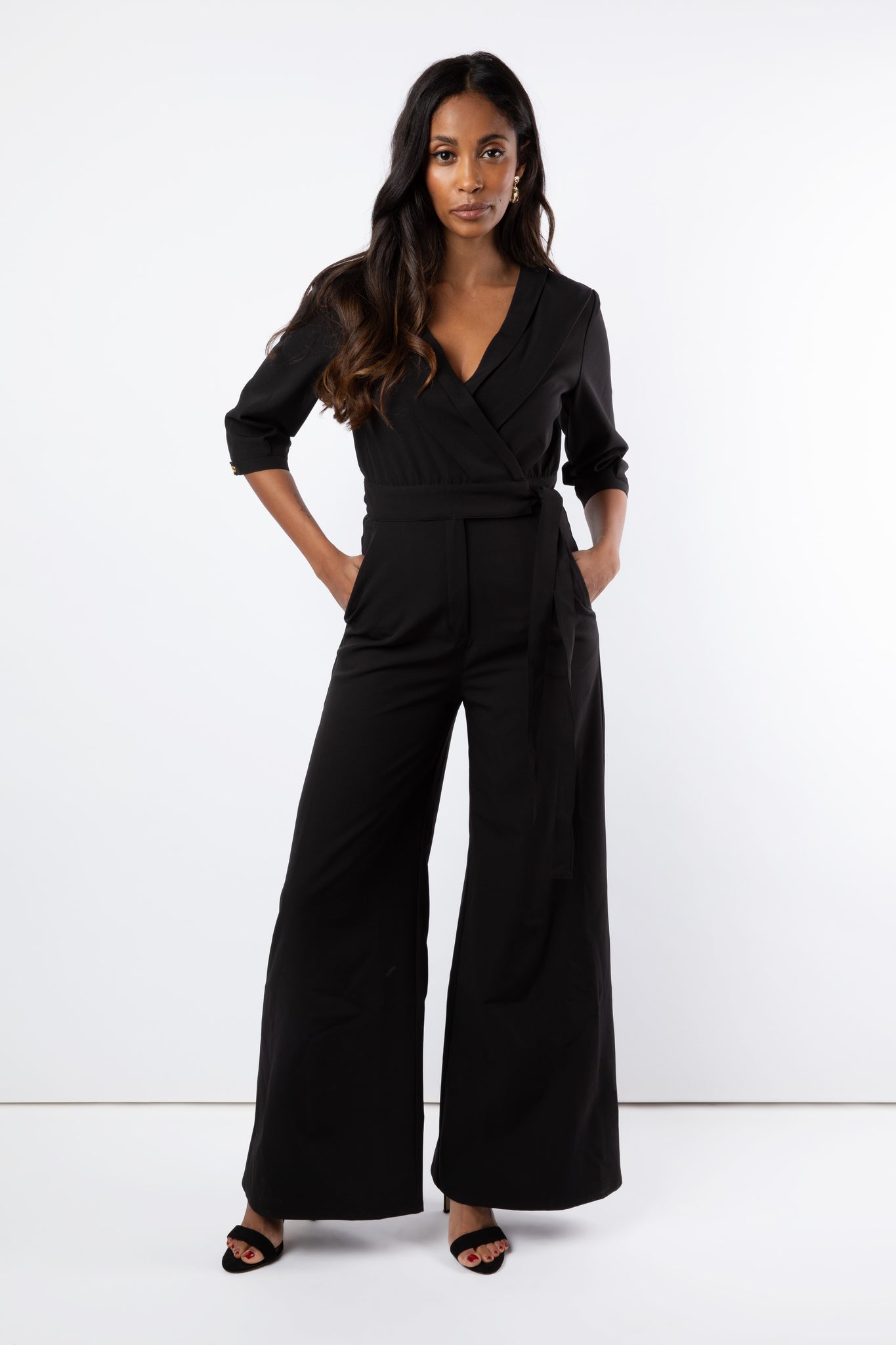 Model wears black jumpsuit with wide leg trouser and tied  belt