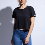 Model wears cropped black boxy fit t-shirt with logo on sleeve and jeans