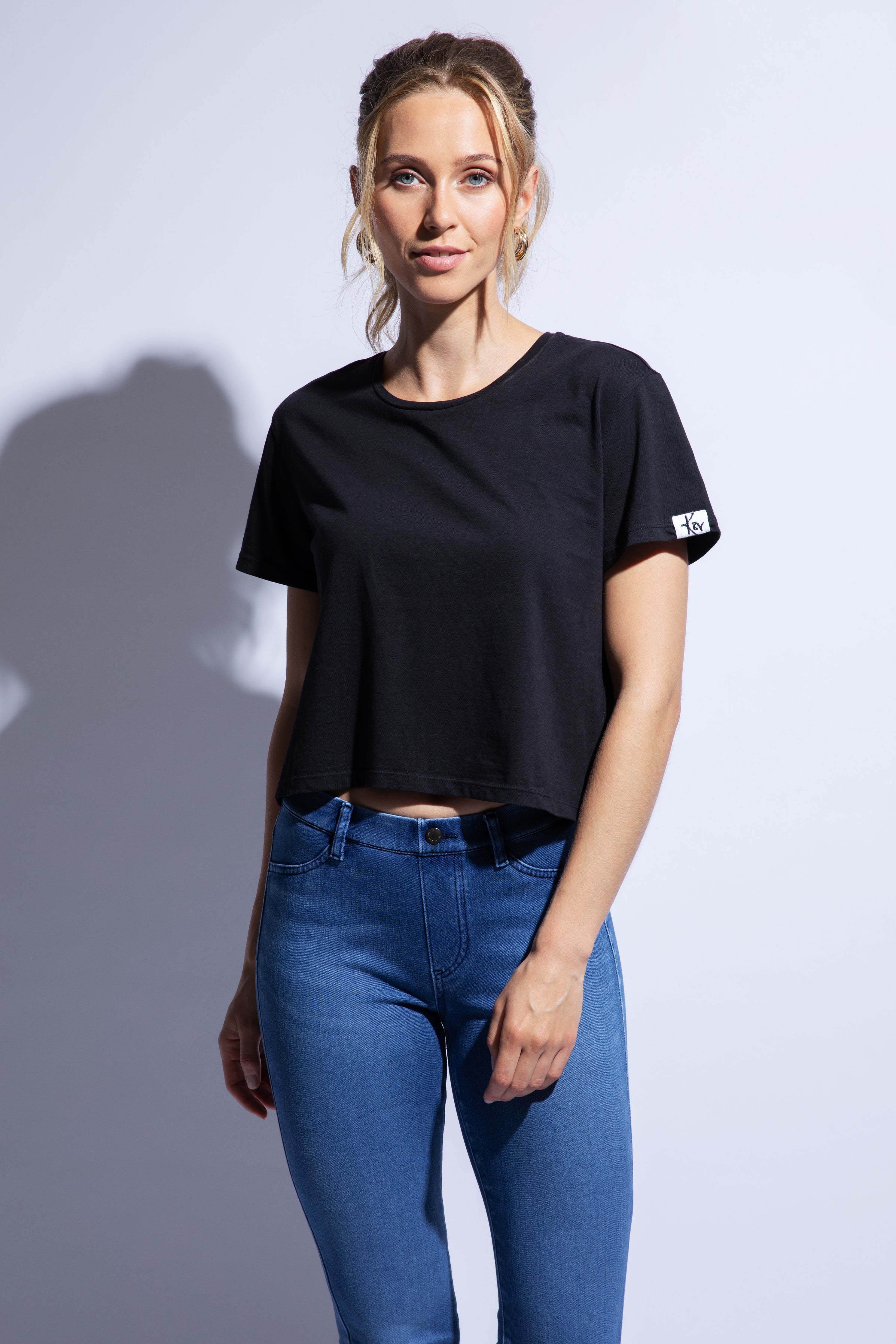 Model wears cropped black boxy fit t-shirt with logo on sleeve and jeans